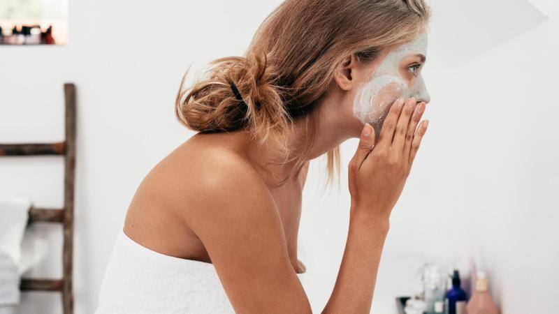 Dívka si v koupelně před zrcadlem nanáší masku na obličej.