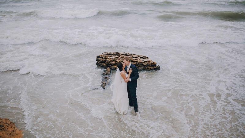 Novomanželé si dávají pusu ve vlnách na pláži, svatební sezona