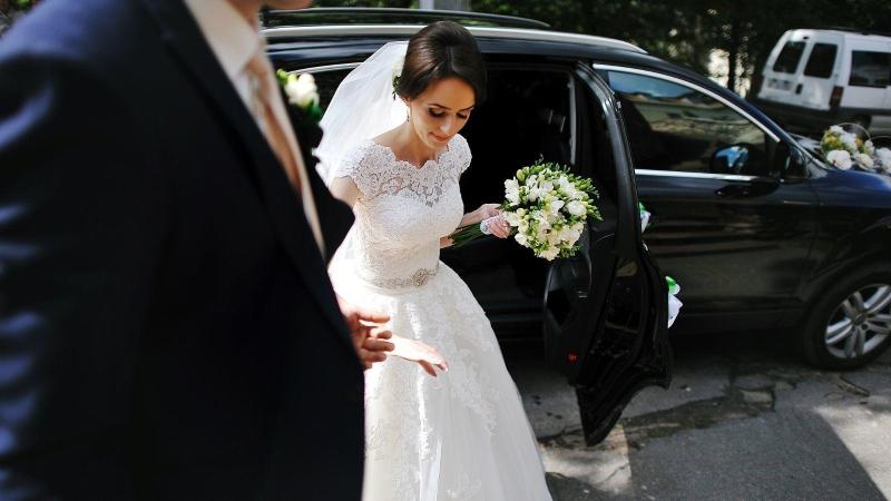 Nevěsta v bílých šatech vystupuje z limuzíny, svatební sezona.