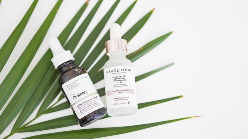2 lahvičky The Ordinary Caffeine Solution 5% + EGCG a Revolution Skincare 5% Caffeine Solution + Hyaluronic Acid na podkladu ze zeleného listu.