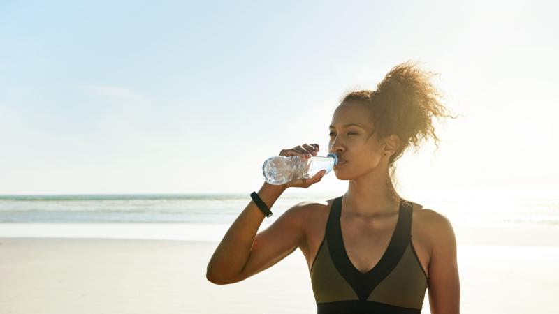Žena na pláži pije vodu.